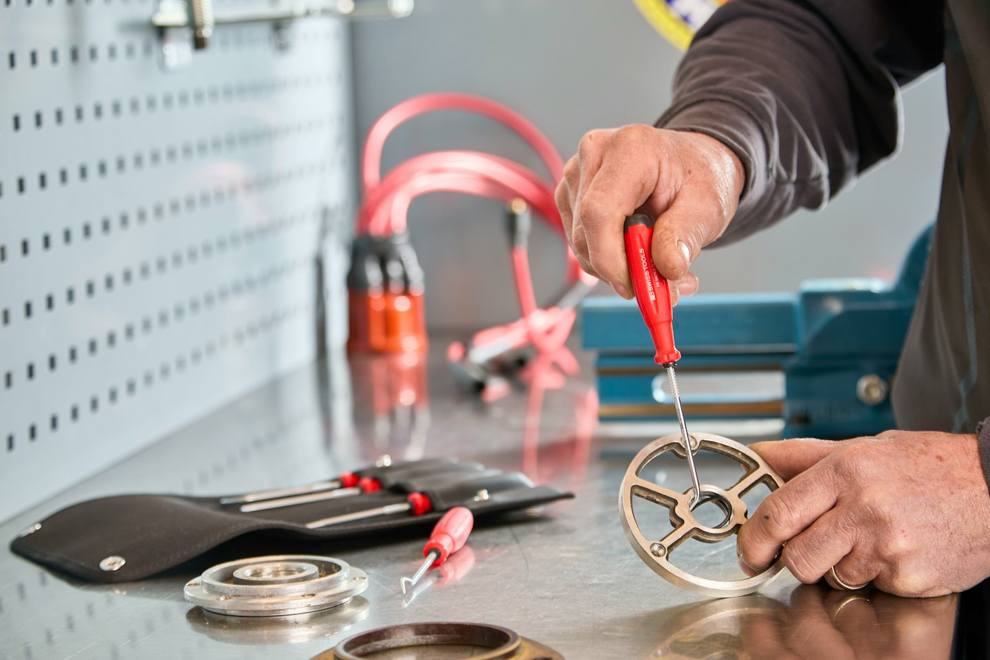 Hands assembling a mechanical part with a red screwdriver.